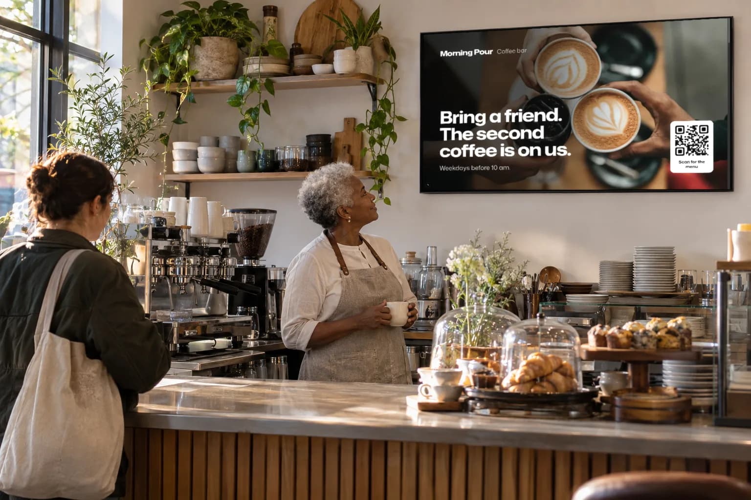 A café owner behind the counter looks up at her own coffee promotion on the wall display